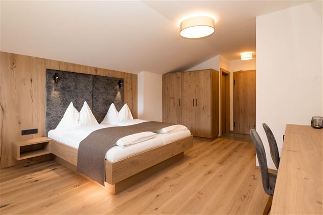 Ein modernes Schlafzimmer mit Holzverkleidung und einem großen Bett. Die gemütliche Atmosphäre wird durch weiche Beleuchtung und einen eleganten Schreibtisch ergänzt.