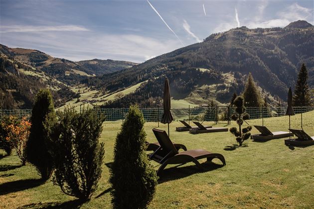 Eine ruhige Landschaft mit Liegen auf einer grünen Wiese. Im Hintergrund sind majestätische Berge unter einem klaren Himmel zu sehen.