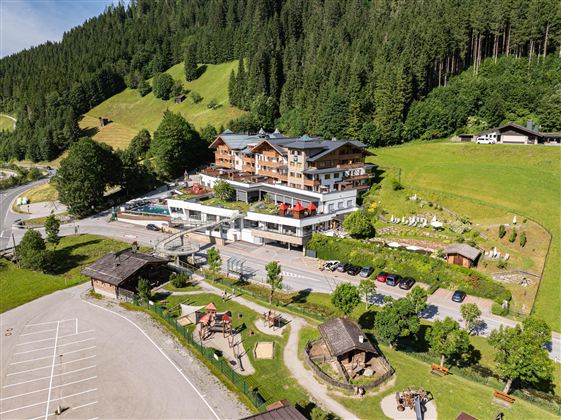 A modern hotel in a picturesque mountain landscape. Surrounded by green forests and a quiet parking lot.