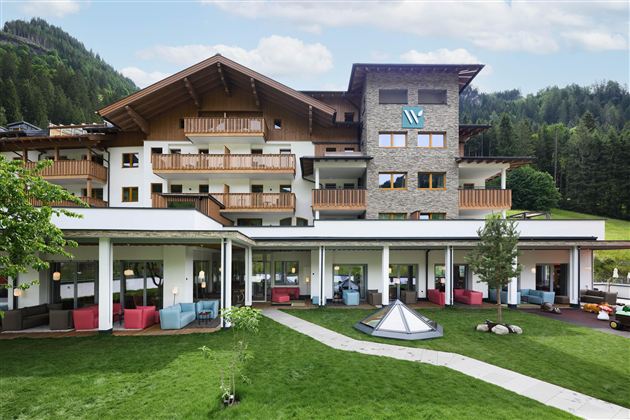 A modern hotel with an attractive outdoor area and balconies. Surrounded by a picturesque mountain landscape and green grass.