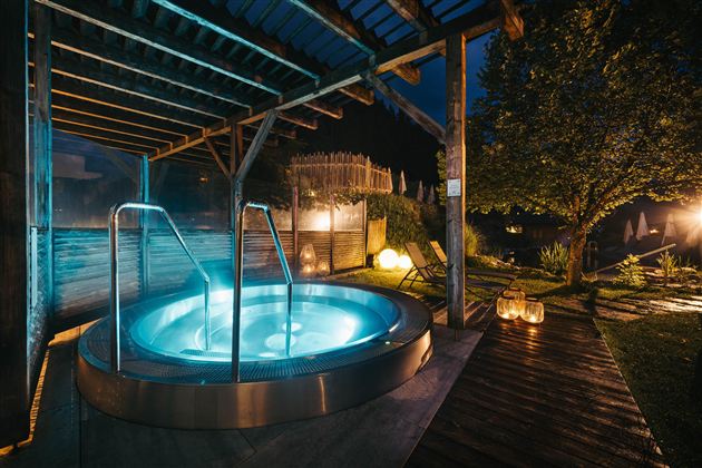 A relaxing hot tub under a covered area. Soft light and a peaceful garden environment create a cozy atmosphere.