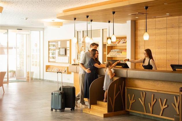 A family checks in at the reception of a hotel. The reception area is furnished in a modern and bright way.