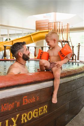A father and his son are playing together in the water. The boy is wearing swim floaties and is smiling happily.
