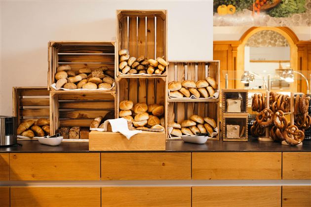 A selection of fresh rolls in wooden boxes on a table. In the background, pretzels are visible in glass containers.