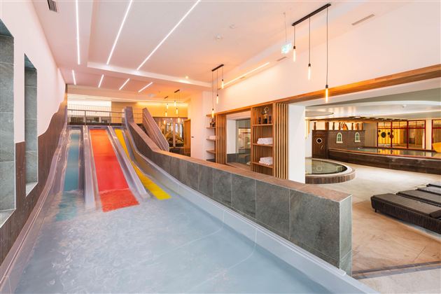 A modern interior with several water slides in different colors. In the background, a pool and sun loungers can be seen.