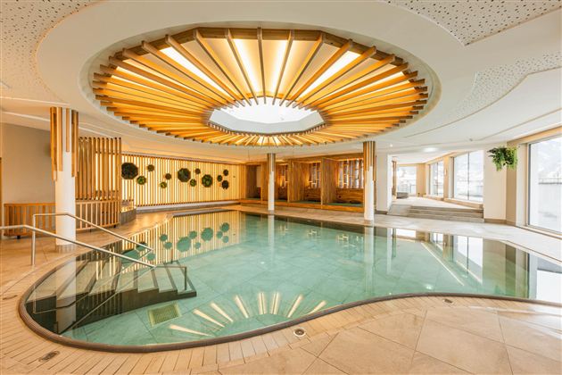 An elegant indoor pool with modern design and warm wooden elements. Natural light streams through the skylight, creating a relaxing atmosphere.
