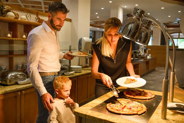 A family is enjoying a meal in a restaurant. The woman is serving pizza while the man and his son are waiting.