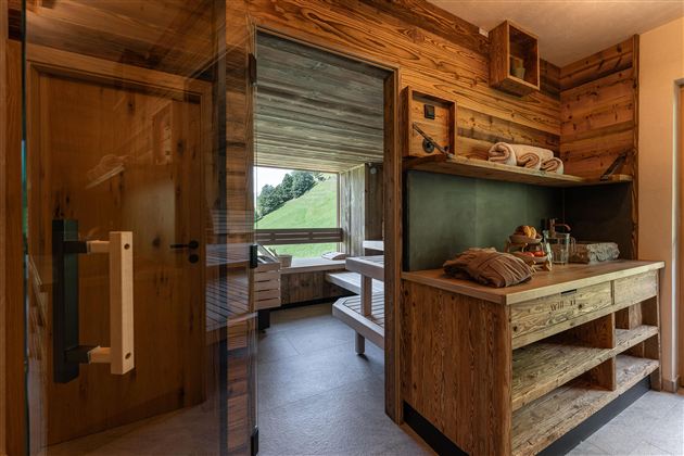 Eine moderne Sauna mit Holzverkleidung und einem angenehmen Ambiente. Große Fenster bieten einen Blick auf die grüne Landschaft.