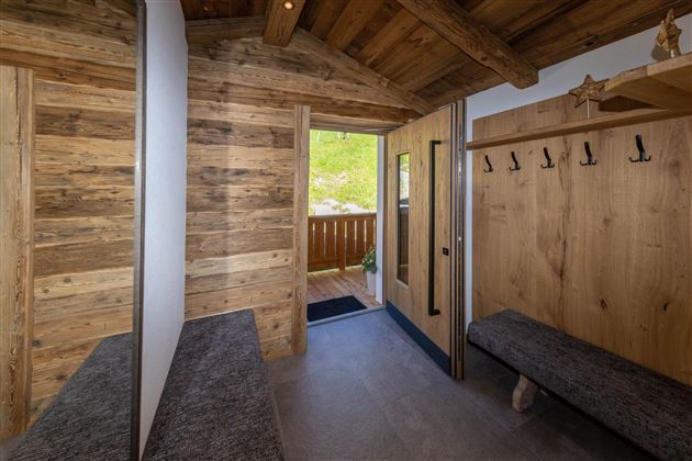 An inviting entrance area with wood paneling and two benches. The view leads to a balcony with green scenery.