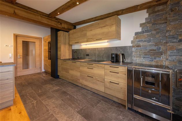 Modern kitchen with wooden furniture and elegant stone walls. It features high-quality appliances and an inviting atmosphere.
