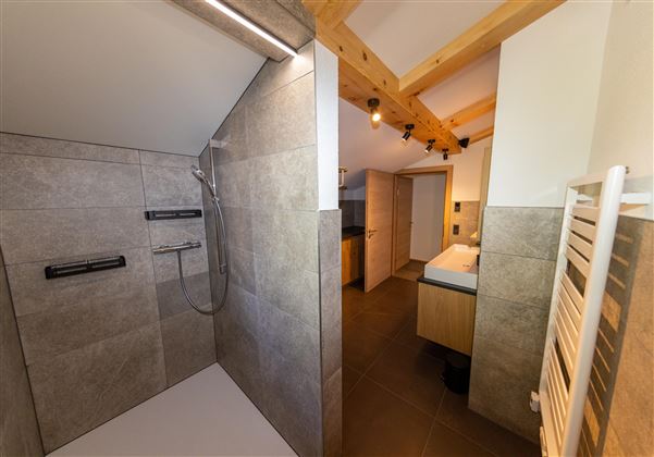 A modern bathroom with a shower and a vanity. The walls are tiled with large, gray tiles.