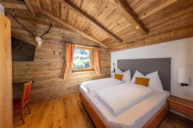 A cozy bedroom with wooden walls and a large window. The two beds are decorated with white bedspreads and orange pillows.