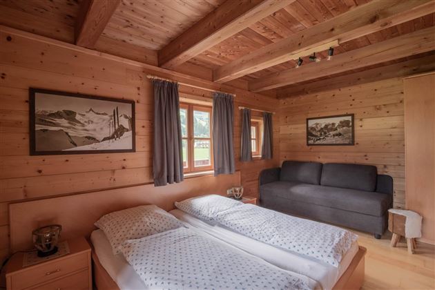Ein gemütliches Schlafzimmer mit Holzwänden und zwei Einzelbetten. Es gibt einen Schlafsofa und große Fenster mit Vorhängen.