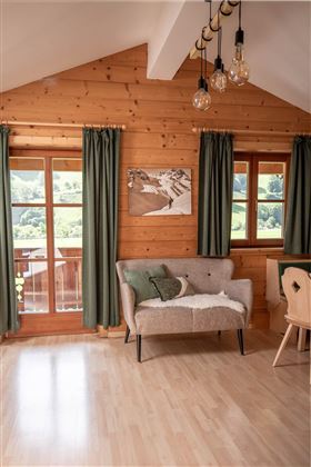 Ein gemütliches Wohnzimmer mit Holzverkleidung und großen Fenstern. Ein beiger Sofa und ein Holztisch verleihen dem Raum eine einladende Atmosphäre.
