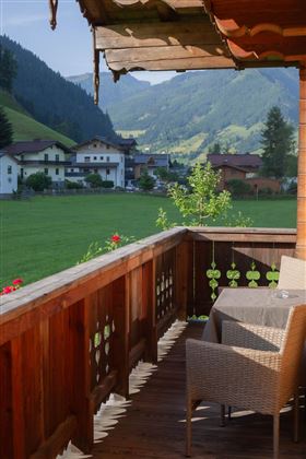 Ein schöner Balkon mit einem Tisch und Stühlen blickt auf eine malerische Landschaft. Im Hintergrund sind Berge und typische alpine Häuser zu sehen.