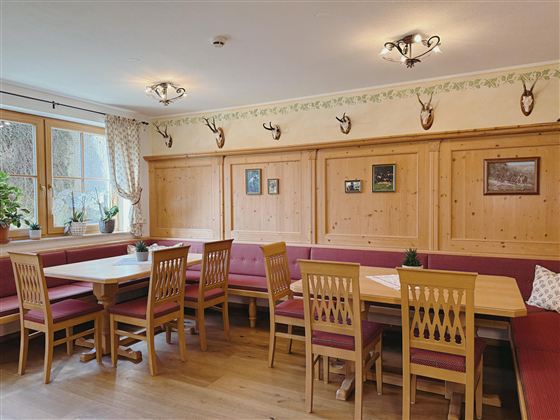A cozy dining area with wooden paneling and red upholstered seats. Pictures and antlers hang on the wall, creating a rustic atmosphere.