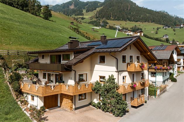 A beautiful house in the mountains with a large balcony and colorful flowers. The surroundings are green and hilly, ideal for a peaceful retreat.