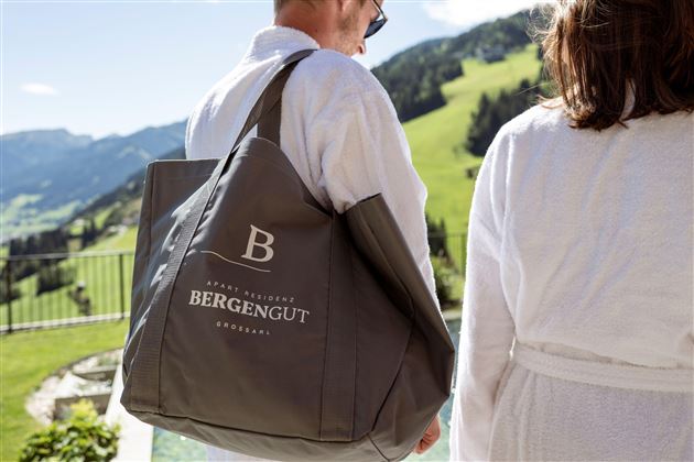 A person is carrying a large bag with the logo "Bergengut". In the background, green hills and a clear sky can be seen.
