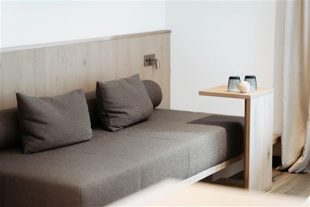 A modern sofa with grey cushions is against a light wall. Next to the sofa is a small table with two glasses and a decorative shell.