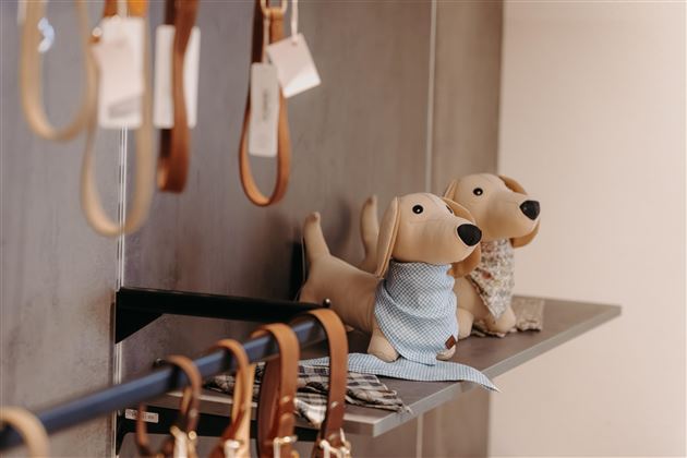 Two plush dog plushies sit on a shelf. Next to them, various leather dog leashes are hanging.