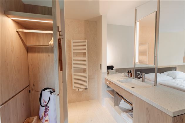 A modern bathroom with wooden shelves and bright lighting. There is a mirror and a clean wash area with personal care products.