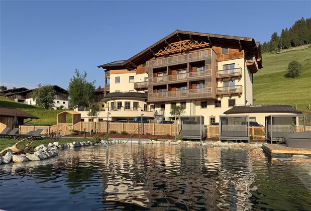 A modern hotel building in the midst of a green landscape. The clear pond reflects the surroundings.