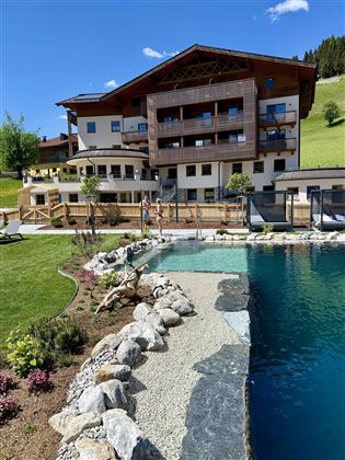 A modern hotel with large balconies and a pool. The surroundings are green and inviting, ideal for a relaxing stay.