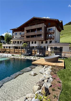 A modern hotel with an outdoor pool and a beautiful garden area. The surroundings are green and provide a tranquil atmosphere.