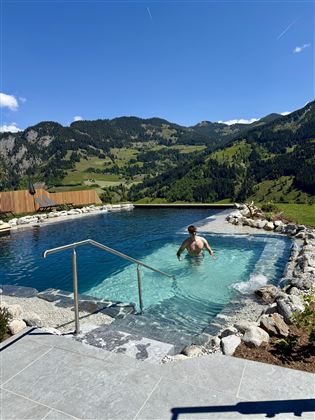 A beautiful pool in the mountains with clear water. In the background, green hills and a blue sky can be seen.