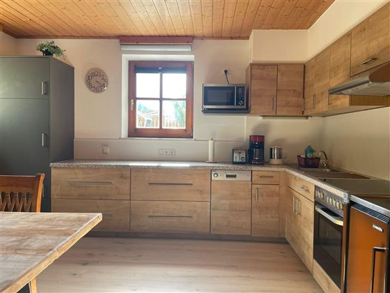 Eine moderne Küche mit Holzfronten und hellen Wänden. Sie ist gut ausgestattet mit Geräten wie einem Herd, einer Mikrowelle und einem Kühlschrank.