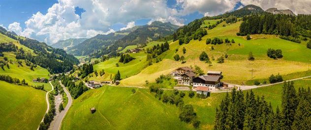 Eine wunderschöne grüne Landschaft mit sanften Hügeln und einem klaren Himmel. Man sieht ein paar Gebäude und eine kurvenreiche Straße in der Umgebung.