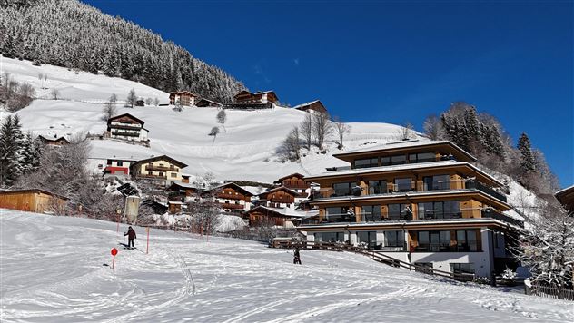 A picturesque mountain village in the snow with traditional houses. In the foreground, skiers can be seen on the slope.
