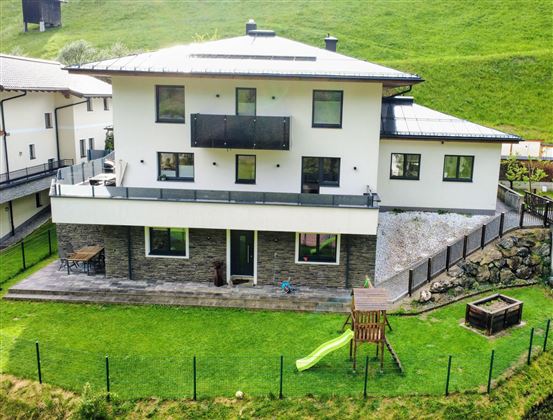 A modern house with a spacious garden. In the foreground, play equipment and a slide can be seen.