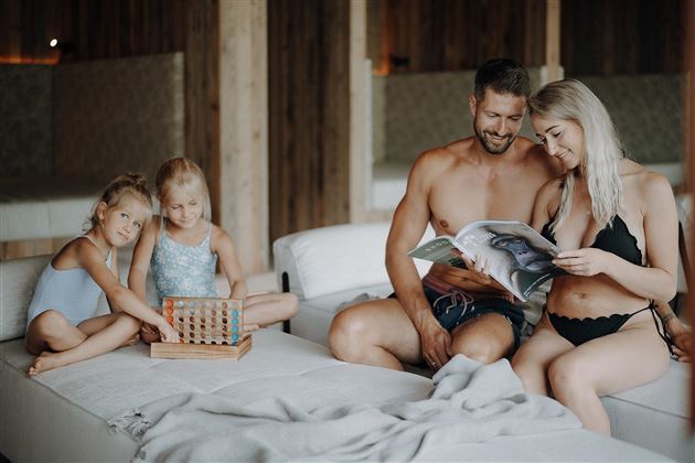 A family is relaxing in a modern room. The children are playing with a toy while the parents are reading a magazine.