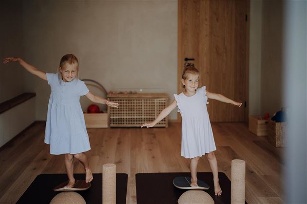 Two girls are standing on balance cushions and practicing their balance. They are wearing light blue dresses and look happy.