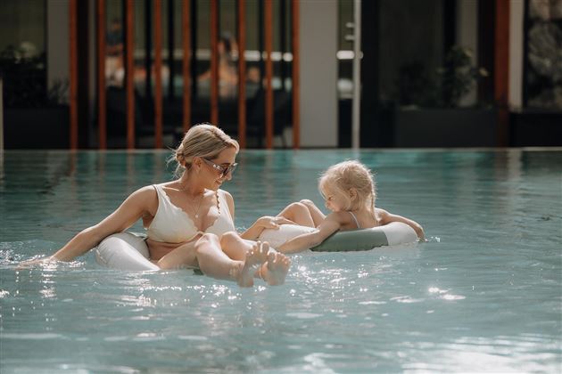 A mother and her child relax in a pool. They are happily playing in the water and enjoying the sun.