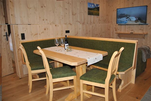 A cozy dining area with a wooden table, benches, and chairs. On the table are glasses and a bottle of wine.