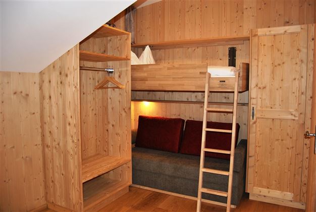 A cozy room with wood paneling. There is a loft bed, a small couch, and a wardrobe.