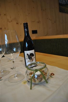 A bottle of wine is standing on a table next to two wine glasses. In a small glass vase, cookies or snacks are decoratively placed.