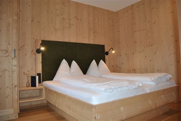 A modern bedroom with wood paneling and a large double bed. The walls are bright and friendly, with stylish wall lamps.