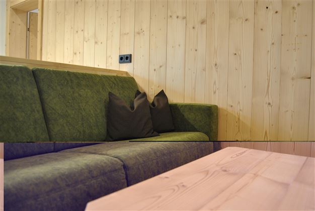 A modern couch in a quiet room with wooden paneling. Cushions are placed on the couch, and a wooden table stands in front of it.