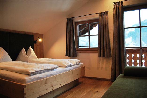 A cozy bedroom with wooden beds and large windows. The atmosphere is warm and inviting, ideal for a relaxing stay.