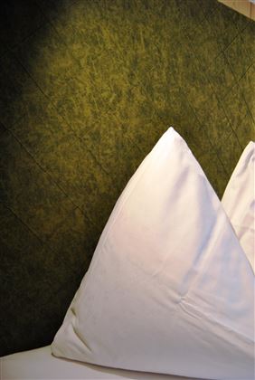 A bedroom with white pillows and a green wall. The pillows are neatly folded and give the room an inviting atmosphere.