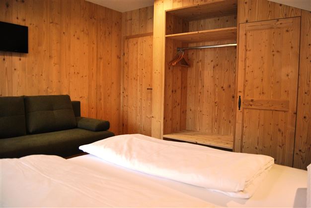 A cozy room with wooden paneling. There is a large bed, a sitting area, and a wardrobe.