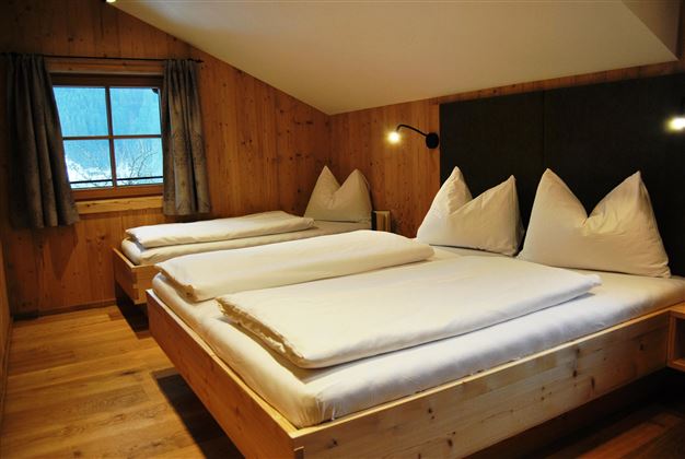 A cozy bedroom with two beds and a window that lets in daylight. The wood-paneled walls create a warm atmosphere.