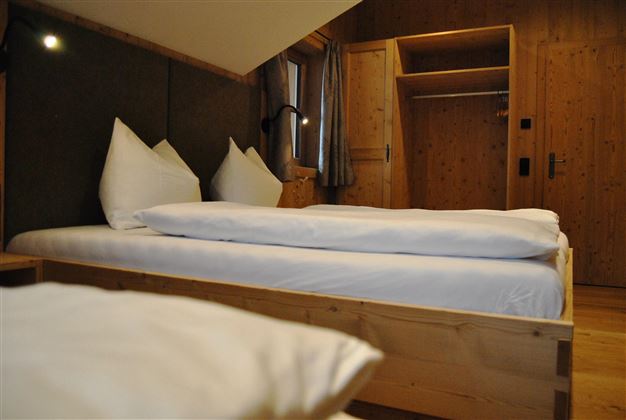 A cozy bedroom with two beds and wooden shelves. The room has a warm atmosphere and is well-lit.