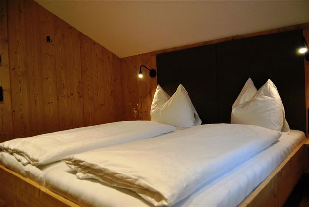 A cozy bedroom with a double bed and two pillows. The walls are made of wood, creating a warm atmosphere.