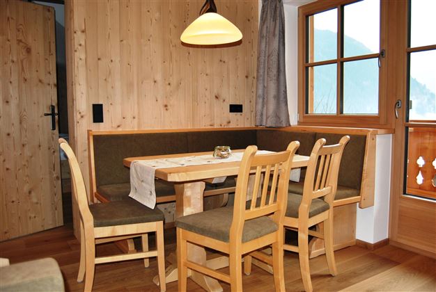 A cozy dining area with wooden walls and a large table. Four chairs surround the table and a window offers a view outside.