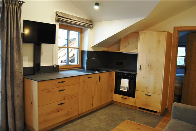 A modern kitchen with wooden cabinets and a dark countertop. The window provides plenty of daylight.
