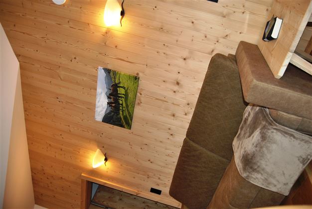 A cozy room with wood paneling and a couch. On the wall hangs a picture of a green landscape.